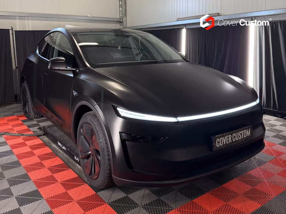 SUV noir mat vu de trois quarts avant, sur un sol à carreaux rouges et noirs devant des rideaux noirs
